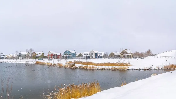 Panorama ram Panorama över en silvlig sjö med avlägsna hus mot molnigt himmel på vintern — Stockfoto
