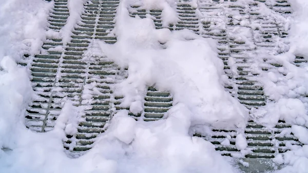 Panorama frame Close up of a metal mesh drainage cover on a road covered with snow