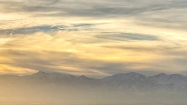 Panorama frame Panorama de uma cidade movimentada contra uma montanha nevada ao pôr-do-sol — Fotografia de Stock