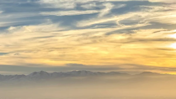 Panorama Panorama de uma cidade movimentada contra uma montanha nevada ao pôr-do-sol — Fotografia de Stock