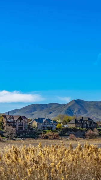 Panorama Bonitas casas frente a un lago con hierbas marrones creciendo en la orilla —  Fotos de Stock