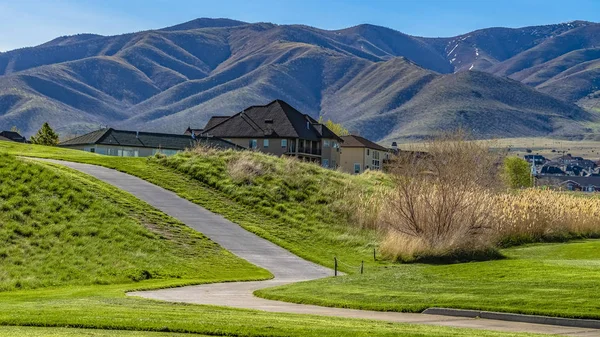 Panorama-Rahmenpanorama einer Straße, die sich an einem sonnigen Tag durch einen mit Gräsern bedeckten Hügel schlängelt — Stockfoto