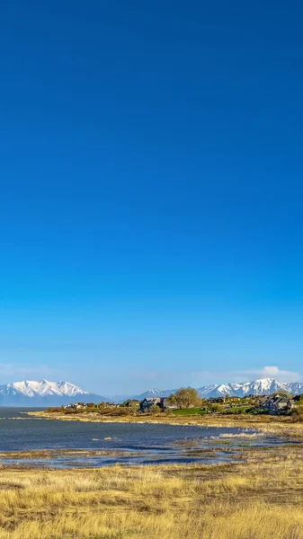 Panorama Vista panorámica de un lago con montaña nevada contra el cielo azul a lo lejos —  Fotos de Stock
