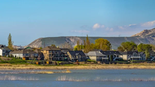 Panorama vue ensoleillée sur les maisons en face d'un lac avec montagne en arrière-plan — Photo