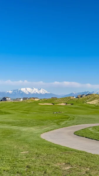 Panorama frame Vast grassy field with a curving paved road and houses beyond the slopes — Stock Photo, Image