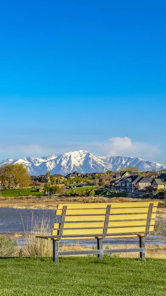 Marco panorámico Banco en un campo cubierto de hierba con vistas al lago y la montaña nevada contra el cielo azul —  Fotos de Stock