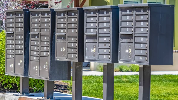 Panorama řady clusterových poštovních schránek s očíslovanými jednotkami na sluncem osvětlovaném chodníku — Stock fotografie