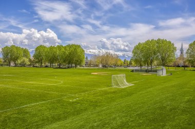 Arka planda yemyeşil ağaçlar ve binalar ile futbol ve beyzbol sahası