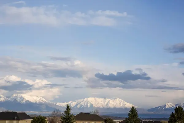 Vista panoramica di un lago e montagna innevata sotto il cielo nuvoloso azzurro pallido — Foto Stock