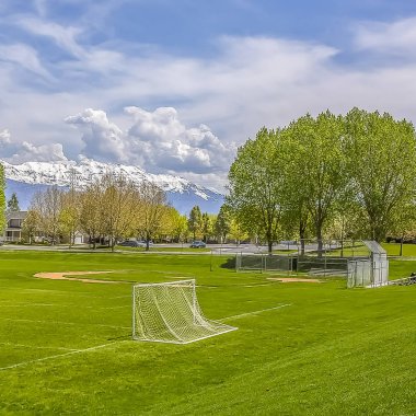 Arka planda yemyeşil ağaçlar ve binalar ile kare futbol ve beyzbol sahası