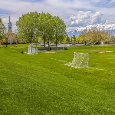 Arka planda yemyeşil ağaçlar ve binalar ile kare çerçeve futbol ve beyzbol alanı
