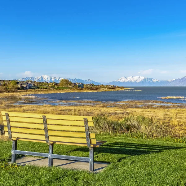 Čtvercové políčko prázdná lavička s výhledem na jezero a vrhá stín na pole za slunečného dne — Stock fotografie