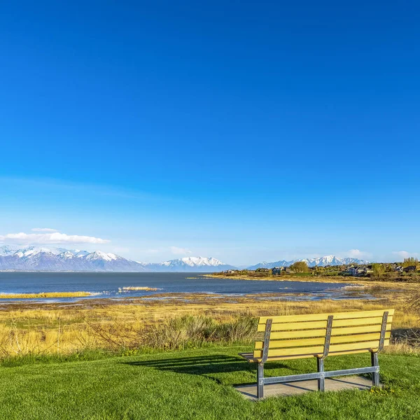 Čtvereček prázdná lavička s výhledem na jezero a vrhá stín na pole za slunečného dne — Stock fotografie