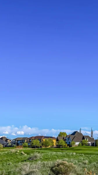 Vertical Gran terreno herboso con casas bajo el cielo azul y nubes hinchadas en un día soleado —  Fotos de Stock