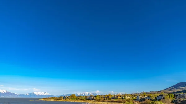 Panorama Vista panorámica de un lago y una montaña cubierta de nieve bajo un cielo azul profundo —  Fotos de Stock