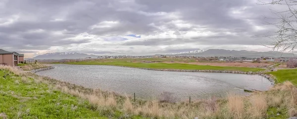 Lago con costa cubierta de hierba con vistas a la montaña distante bajo el cielo nublado —  Fotos de Stock