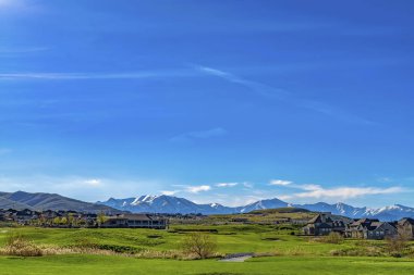 Güneşli bir günde uçsuz bucaksız mavi gökyüzünün altında otlarla kaplı arazi üzerine inşa edilmiş evler