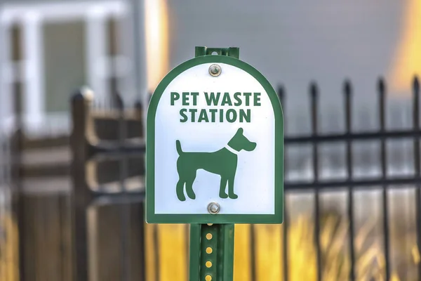 Close up of a Pet Waste Station with gate and building in the blurry background