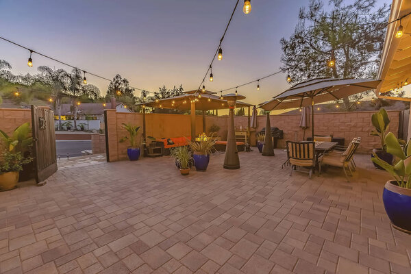 Столовая и гостиный уголок на каменном кирпичном патио, освещенном струнными огнями
