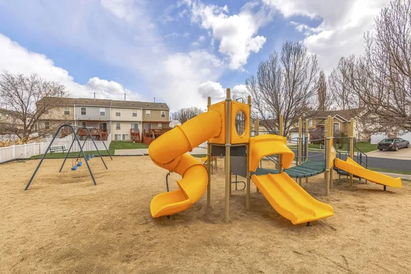 Playground in the middle of houses and roads under blue sky filled with clouds