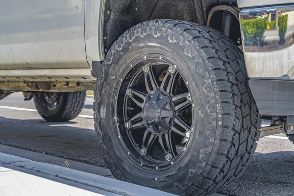 Black rubber wheel of a silver vehicle parked on the road on a sunny day — Stock Photo, Image