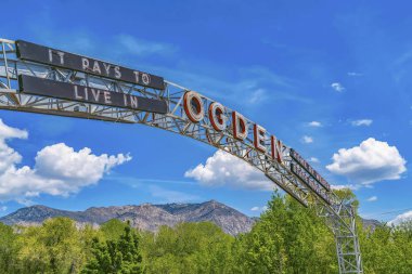 The welcome arch in Ogden Utah against vibrant trees and towering mountain clipart