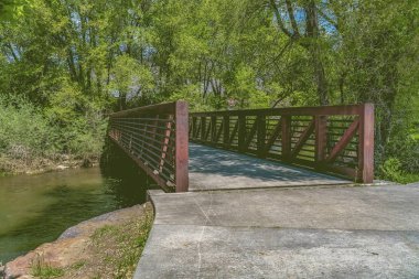 Güneşli bir günde mavi gökyüzüne karşı yemyeşil ağaçlarla çevrili bir gölün üzerindeki köprü