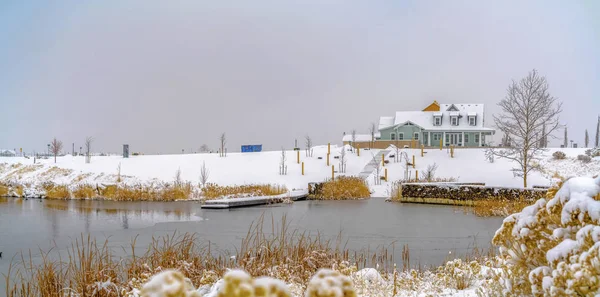 Escénica vista de invierno de un lago tranquilo con una hermosa casa cerca de la orilla nevada — Foto de Stock