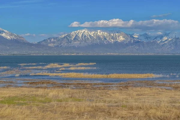 Snowy mountain towering over the valley and lake that reflects the blue sky