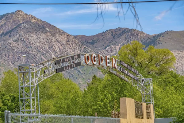 Welcome arch in Ogden Utah against lush trees towering mountain and blue sky