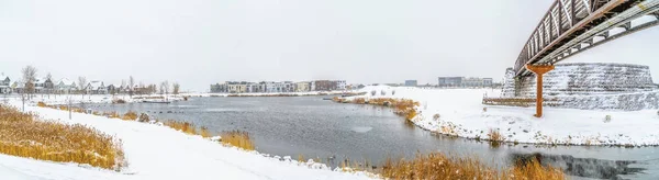 Lac et bâtiments entourés de sol enneigé sous un ciel nuageux en hiver — Photo
