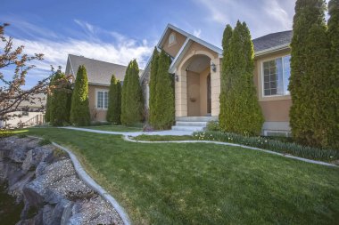 Mavi gökyüzü ve bulutlar altında ev cephesinde Yard ve konik şekilli ağaçlar