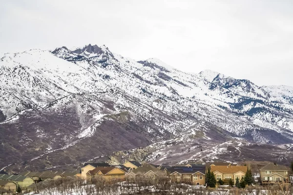 Жилой район у подножия возвышающейся снежной горы против облачного неба — стоковое фото