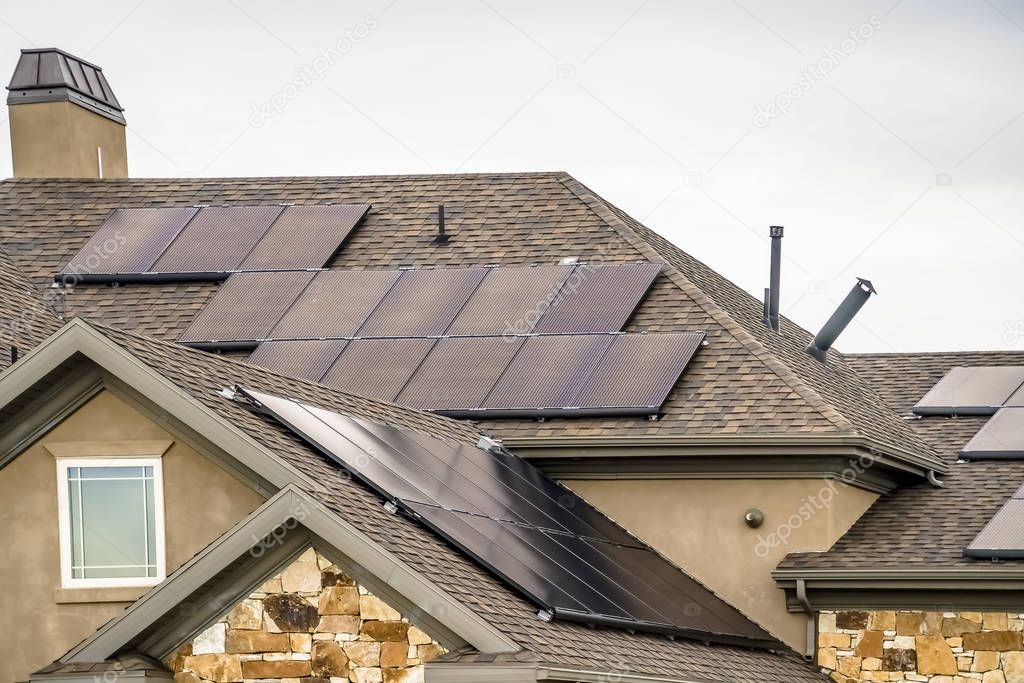 Solar panels on the dark pitched roof of a home with stone and concrete wall