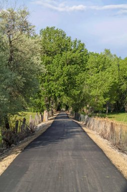 Yol çimenli bir arazi ortasında ve bulutlu gökyüzü altında zincir bağlantı çit ile kaplı