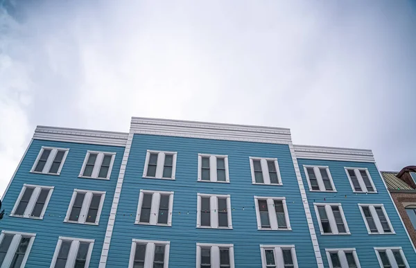 Building exterior with blue wall and vertical sliding windows against cloudy sky