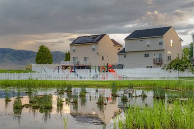 Oyun alanları evleri bulutlu gökyüzü ve çit yansıması ile parlak çimenli gölet