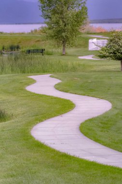 Arka planda bir gölet ve tezgah ile çimenli arazi ile eğri yol