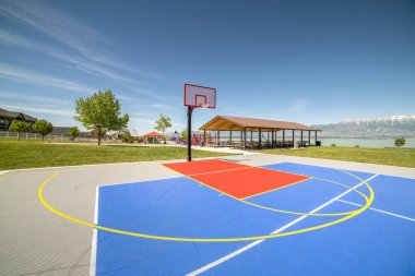 Arka planda piknik köşkü ve oyun alanı bulunan açık basketbol sahası