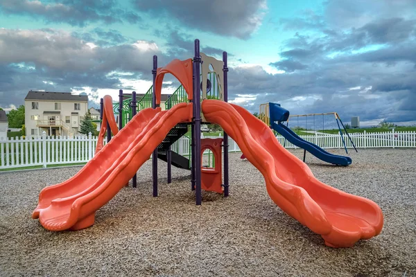 Colorful slides and swings on a neighborhood playground under cloudy blue sky