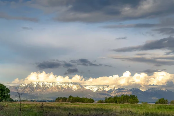 Malownicza przyroda z nasłonecznienia śnieżnej góry i pochmurne niebo nad jeziorem i doliną — Zdjęcie stockowe