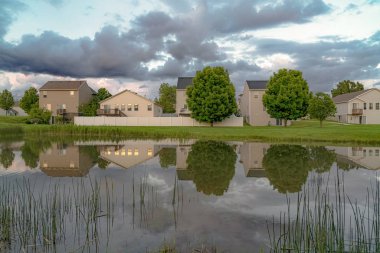 Çok katlı evlerin yansıması ile Gölet yemyeşil ağaçlar ve bulut dolu gökyüzü