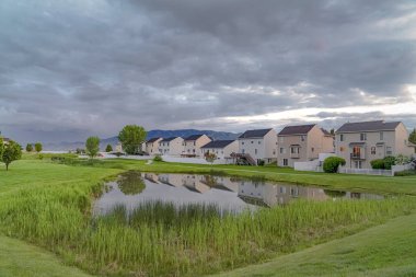 Balkonlu güzel evlerin önünde çimenli bir parkta köprü ile parlak gölet