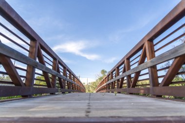 Güneşli bir günde mavi gökyüzüne karşı bir köprünün ahşap güverte ve paslı korkulukları