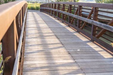 Güneşli bir günde ahşap güverte ve kahverengi kafes korkuluk ile bir köprü kapatın