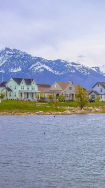 Dikey uzun çerçeve Dağ ve bulutlu gökyüzüne karşı kıyıya yakın evleri ile bir göl Manzara görünümü
