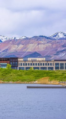 Dikey çerçeve Binalar ve bulutlu bir günde bir gölün çimenli kıyısı ötesinde karlı dağ