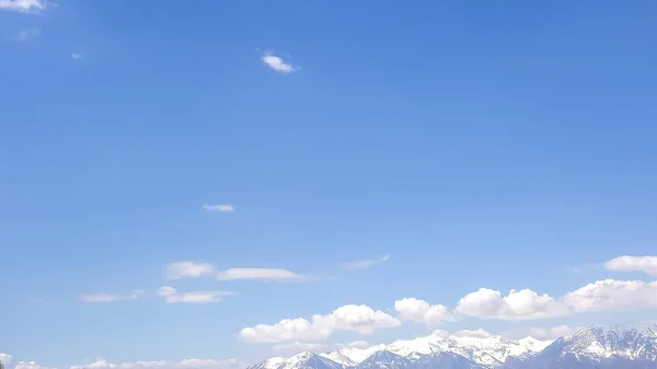 Panorama frame enorme blauwe hemel met gezwollen witte wolken over een berg met besneeuwde piek — Stockfoto