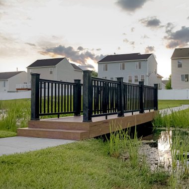 Gün batımında bir ağaç evler ve coudy gökyüzü manzaralı küçük bir gölet üzerinde Square Bridge