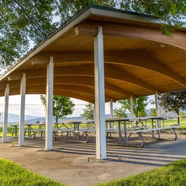 Güneşli bir günde manzaralı bir parkta bir pavyon altında Kare Piknik masaları ve banklar